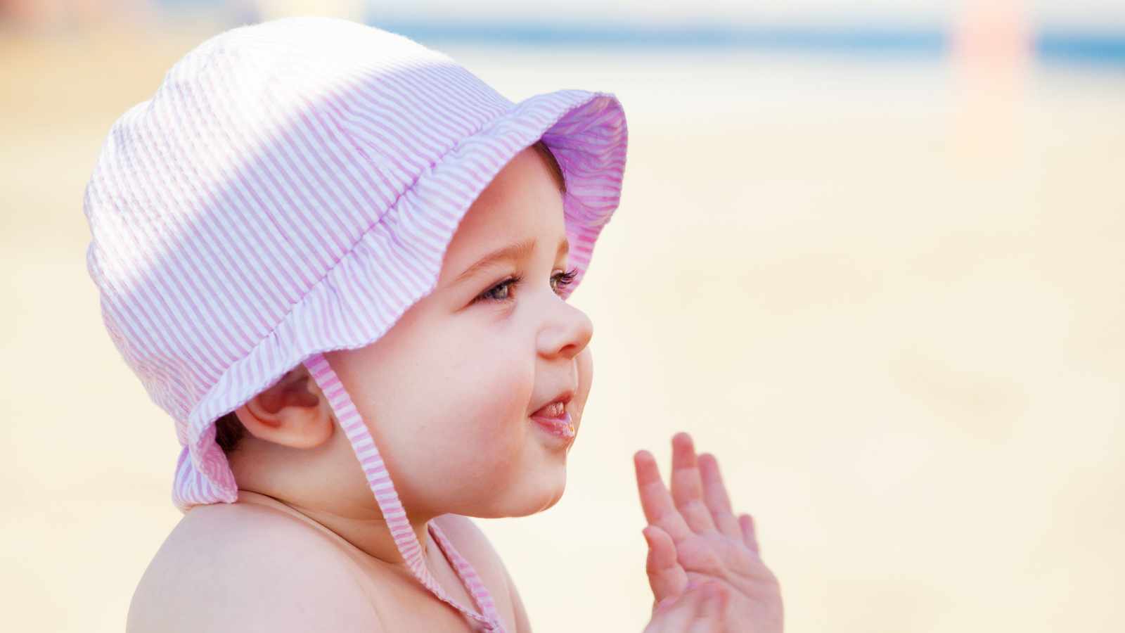 A baby wearing a striped sun hat is looking and smiling to the side.