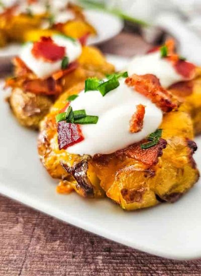 A plate of loaded smashed potatoes topped with sour cream, bacon bits, and chopped green chives.