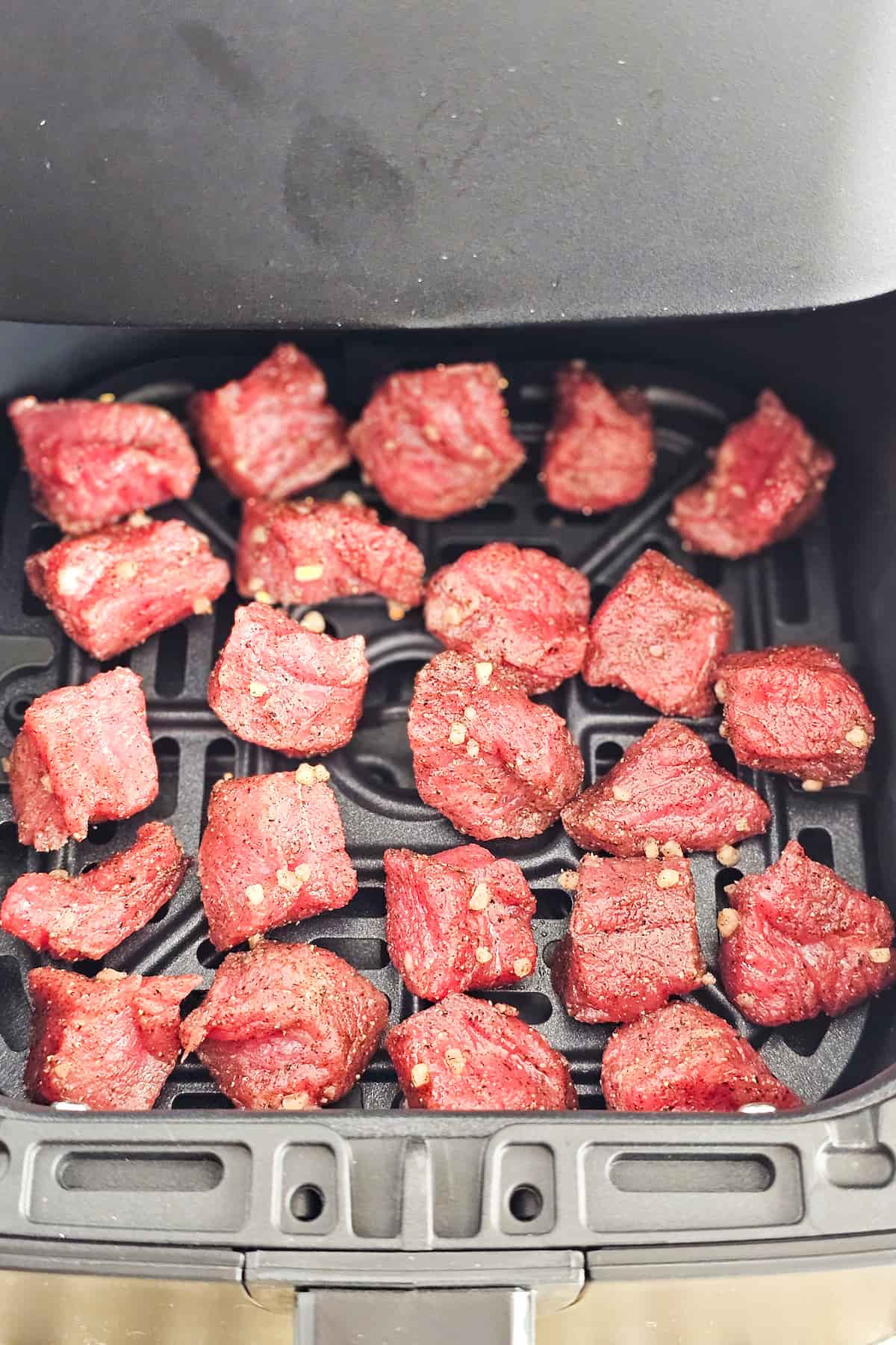 Air fryer steak bites, seasoned to perfection, are arranged on the air fryer basket ready for cooking.