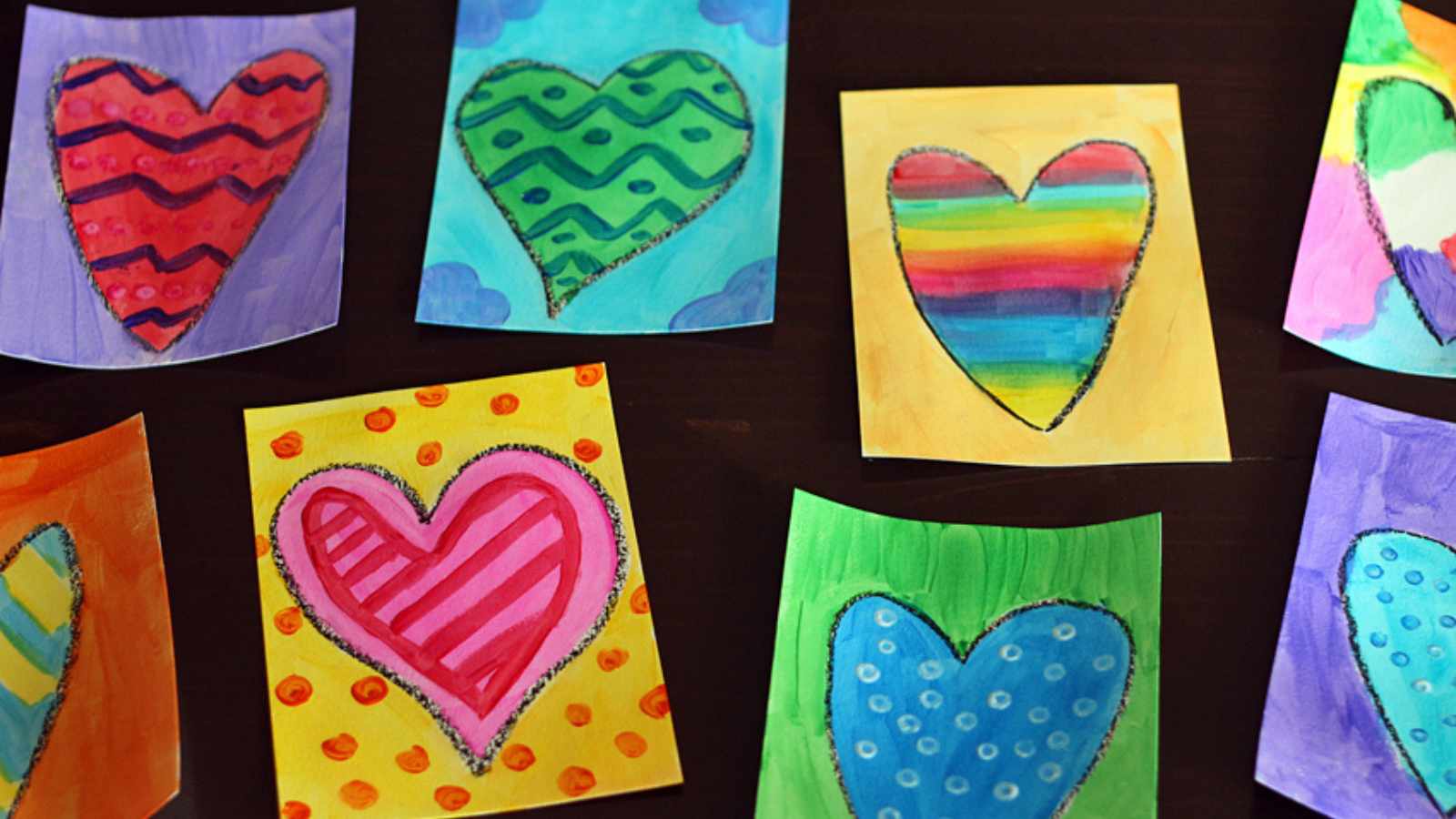 Colorful heart paintings on rectangular pieces of paper, each featuring different patterns and backgrounds, displayed on a dark surface.