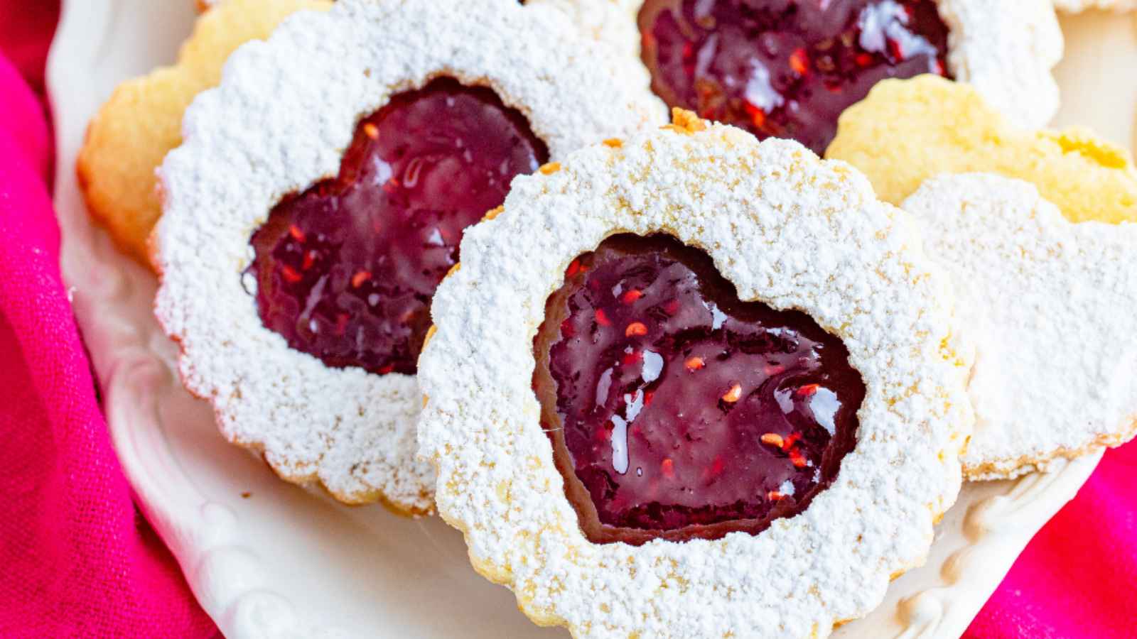 A batch of golden-brown Air Fryer Linzer Cookies with raspberry preserves filling, dusted with powdered sugar.