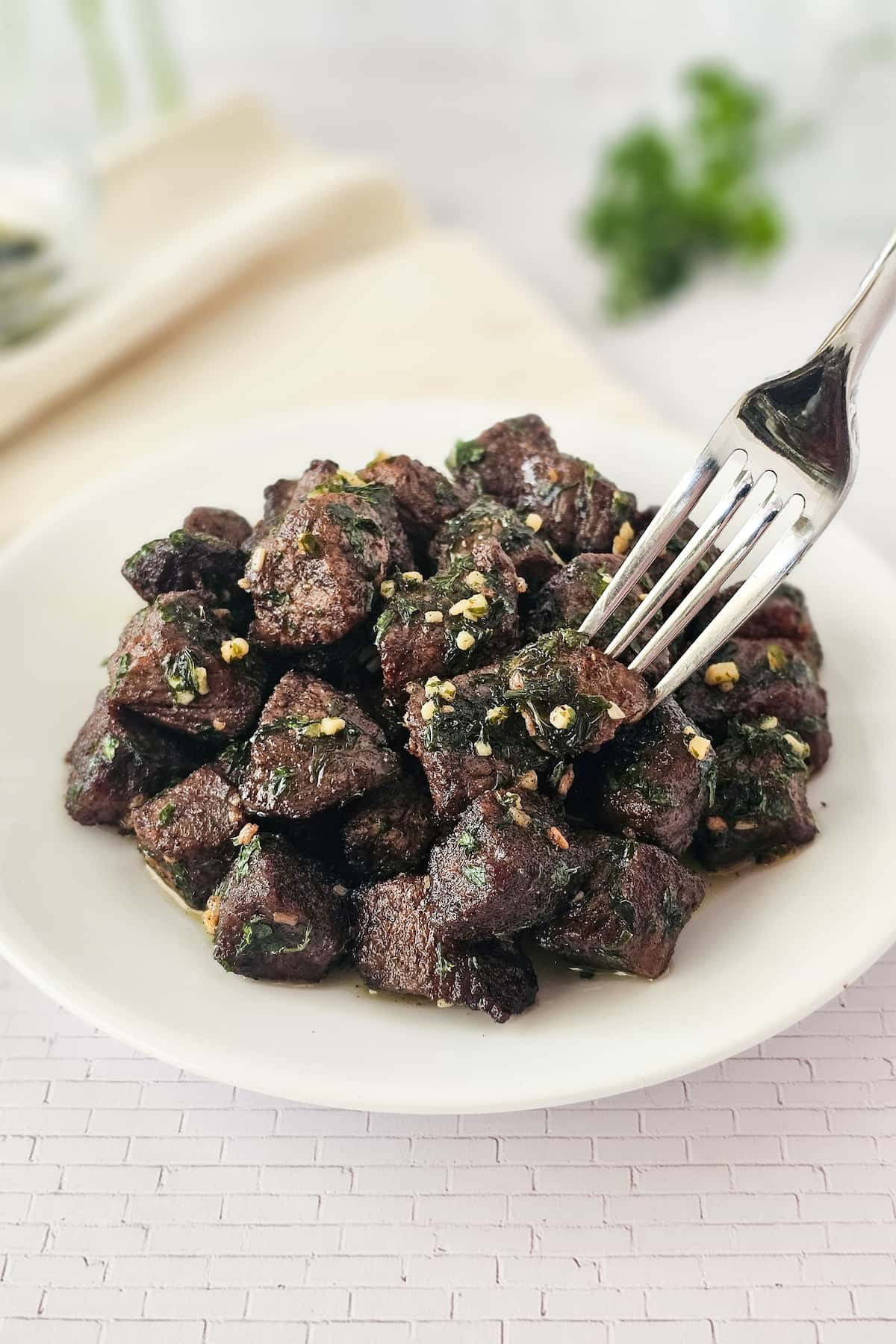 A fork rests on a white plate filled with air fryer steak bites.