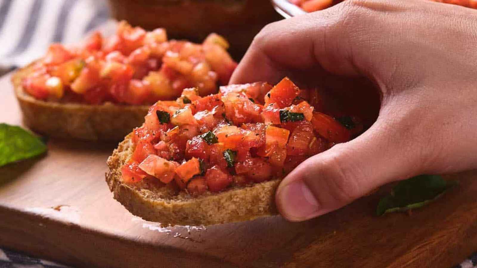 A person's hand picking up a slice of bruschetta al pomodoro.