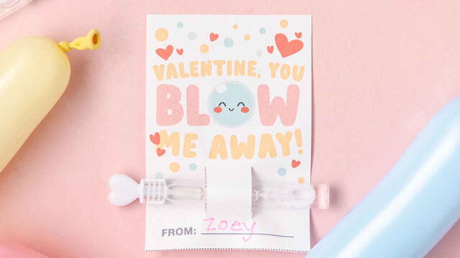 Colorful Valentine's card with text "Valentine, you blow me away!" surrounded by balloons. A small bubble wand is attached below.