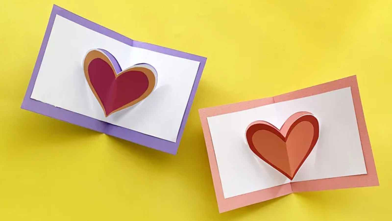 Two open handmade cards feature 3D heart shapes against a yellow background. One card has a purple border, and the other has a pink border.
