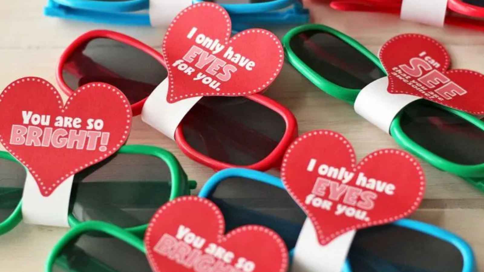 Colorful sunglasses with heart-shaped tags featuring Valentine's messages like "You are so bright!" and "I only have eyes for you.