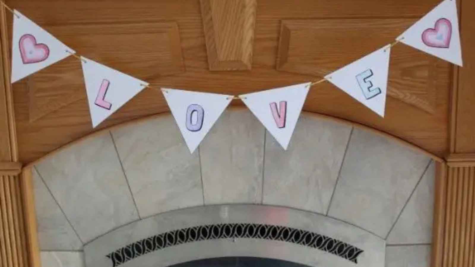 A triangular banner hangs on a wooden door, spelling "LOVE" with hearts on the first and last pennants.
