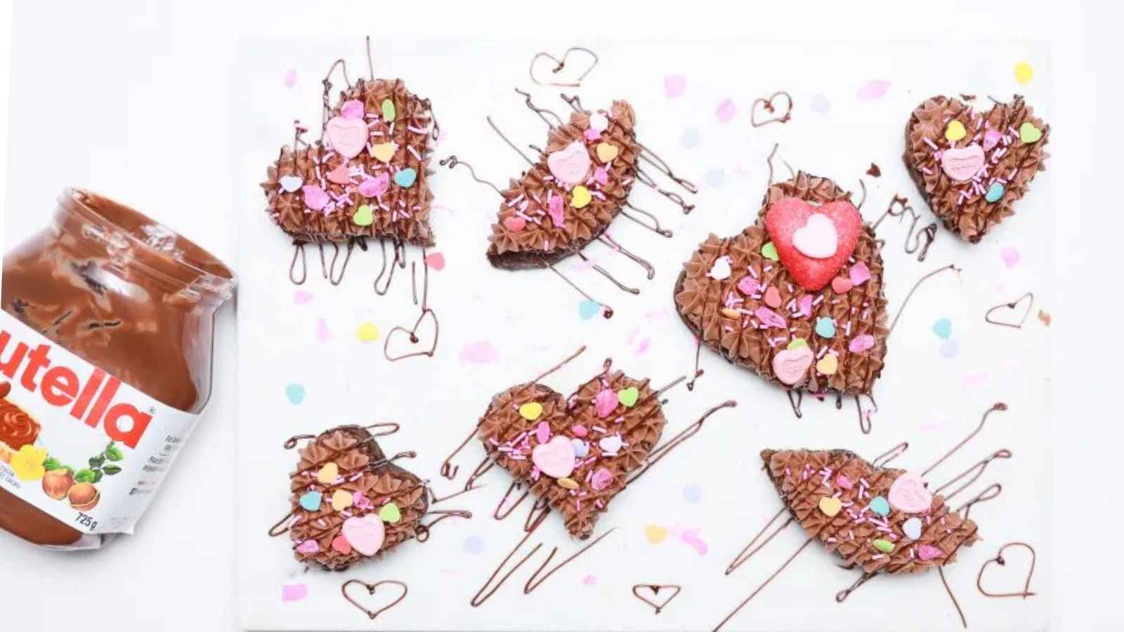 Heart-shaped chocolate treats with colorful sprinkles and icing on a white surface.