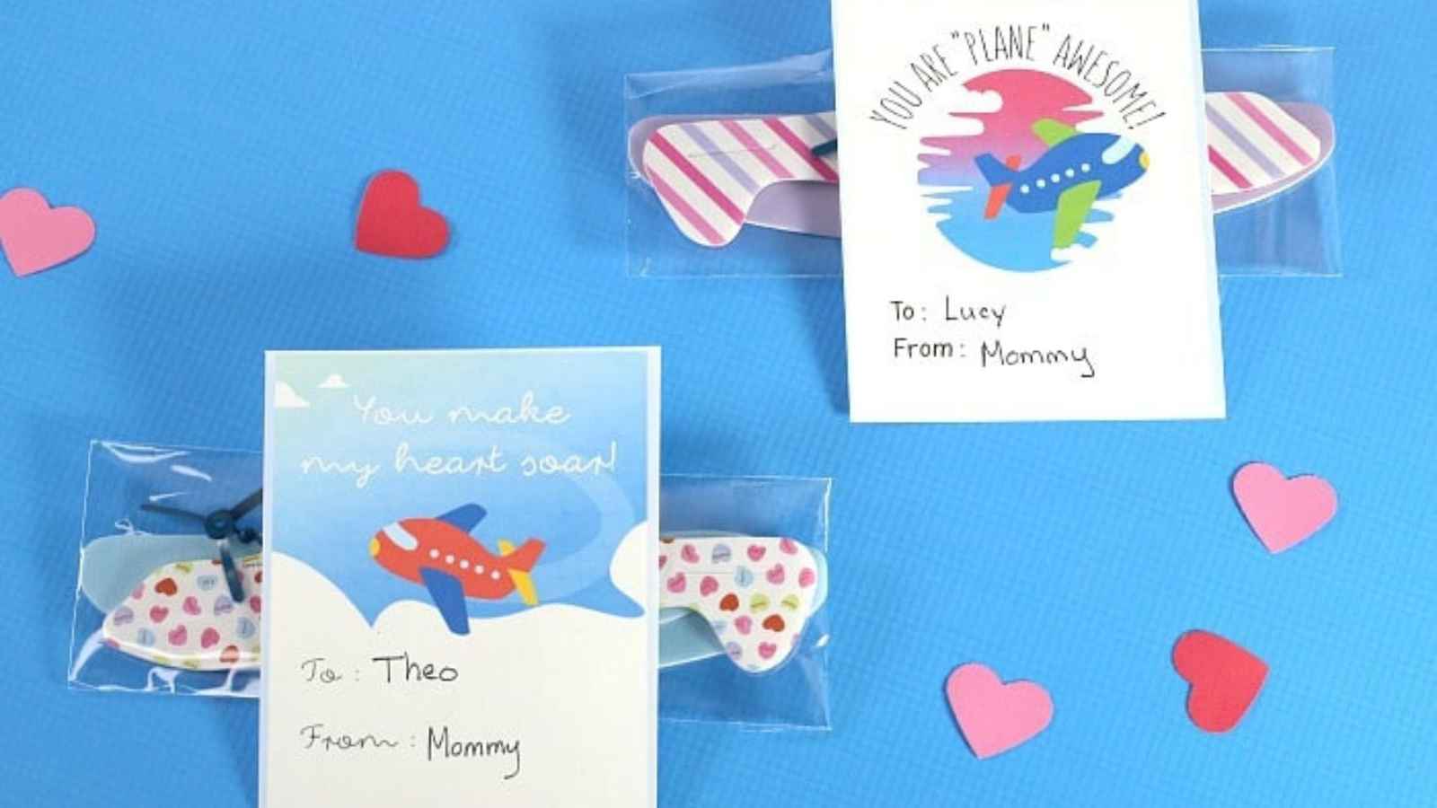 Two airplane-themed Valentine's Day cards with candies on a blue background, surrounded by paper hearts. Cards are addressed to Theo and Lucy from Mommy.