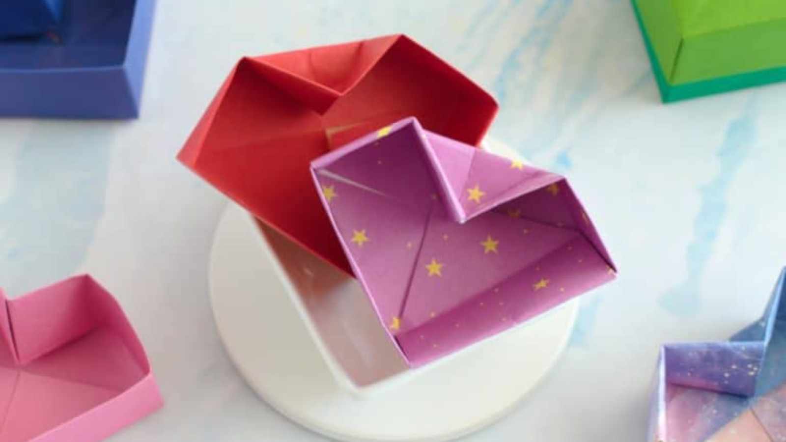 Origami heart boxes in various colors, including red and purple with star patterns, displayed on a white surface.