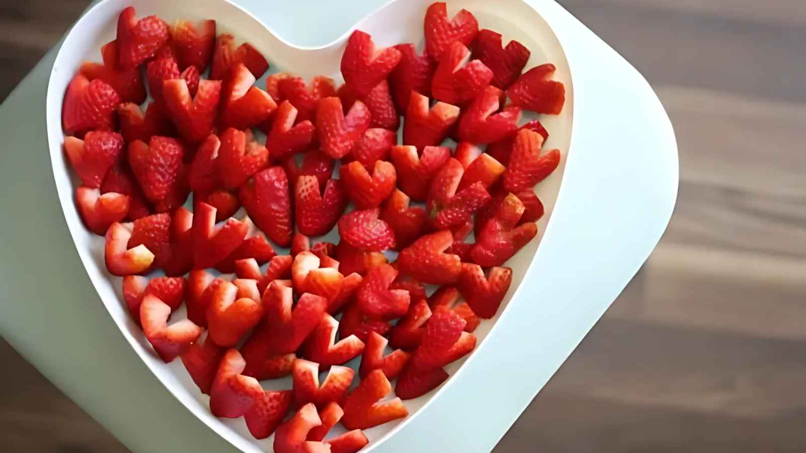 Heart-shaped plate filled with sliced strawberries on a table.