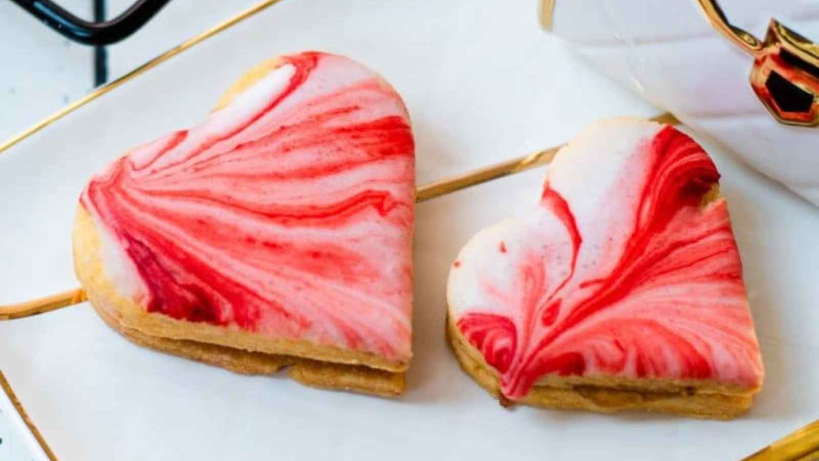 Two heart-shaped cookies with red and white marbled icing on a white tray.