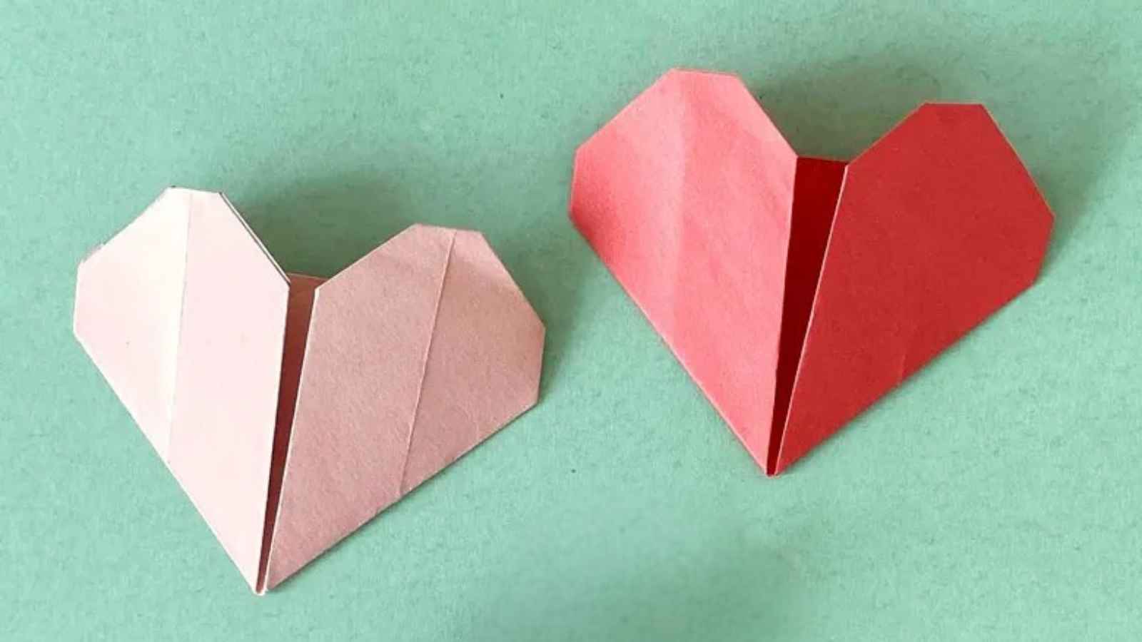 Two origami hearts, one pink and one red, on a light green background.