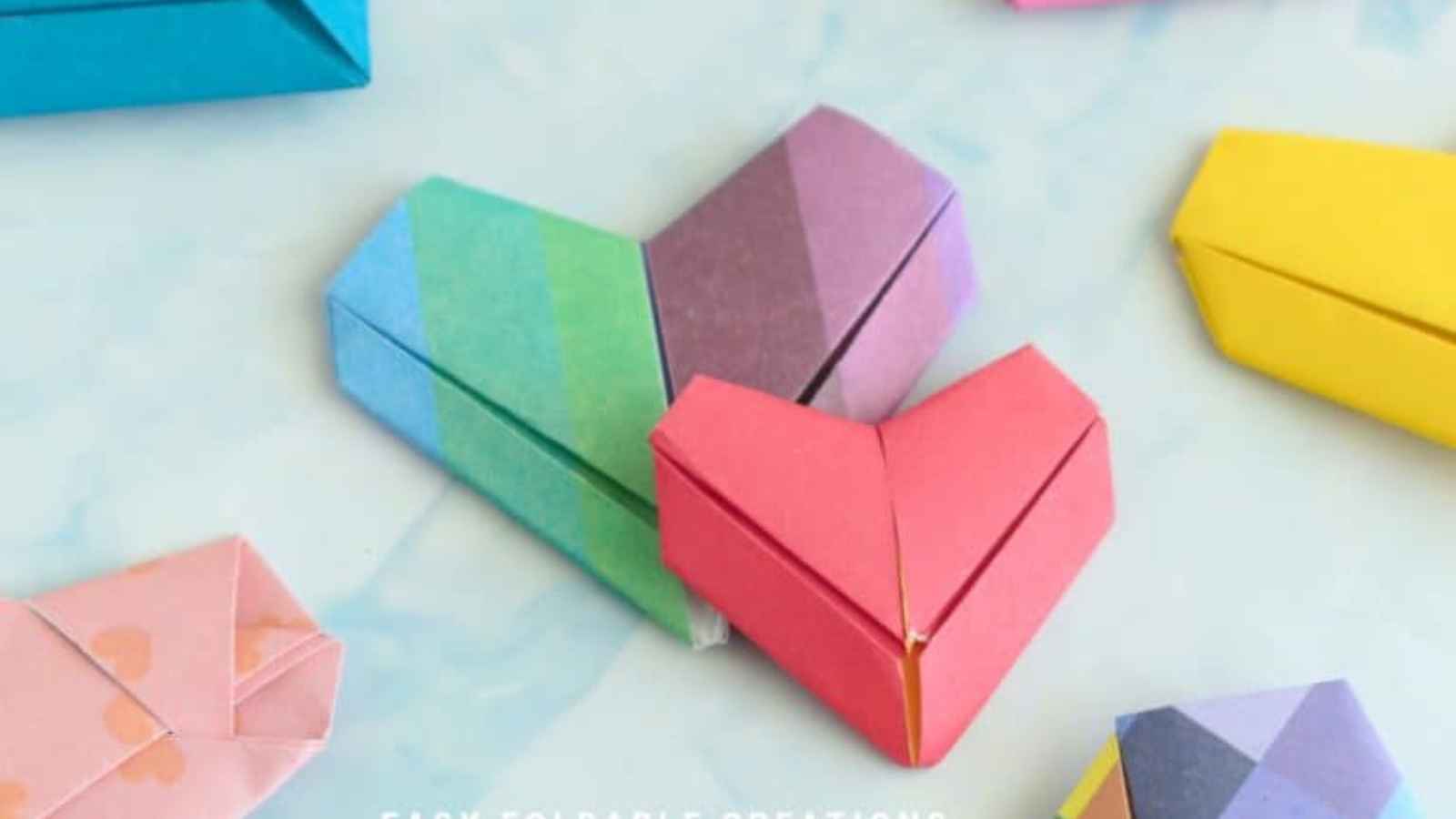 Colorful origami paper hearts scattered on a light blue surface.