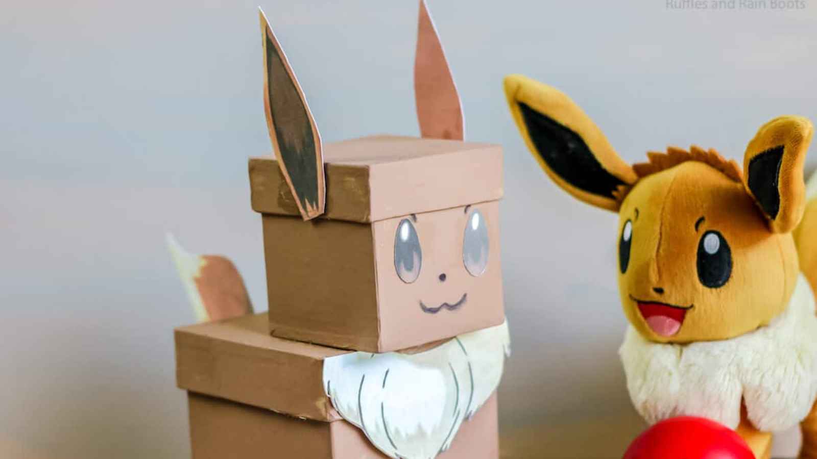 Crafted cardboard and plush toys resembling animals with large ears, positioned near a red ball on a flat surface.