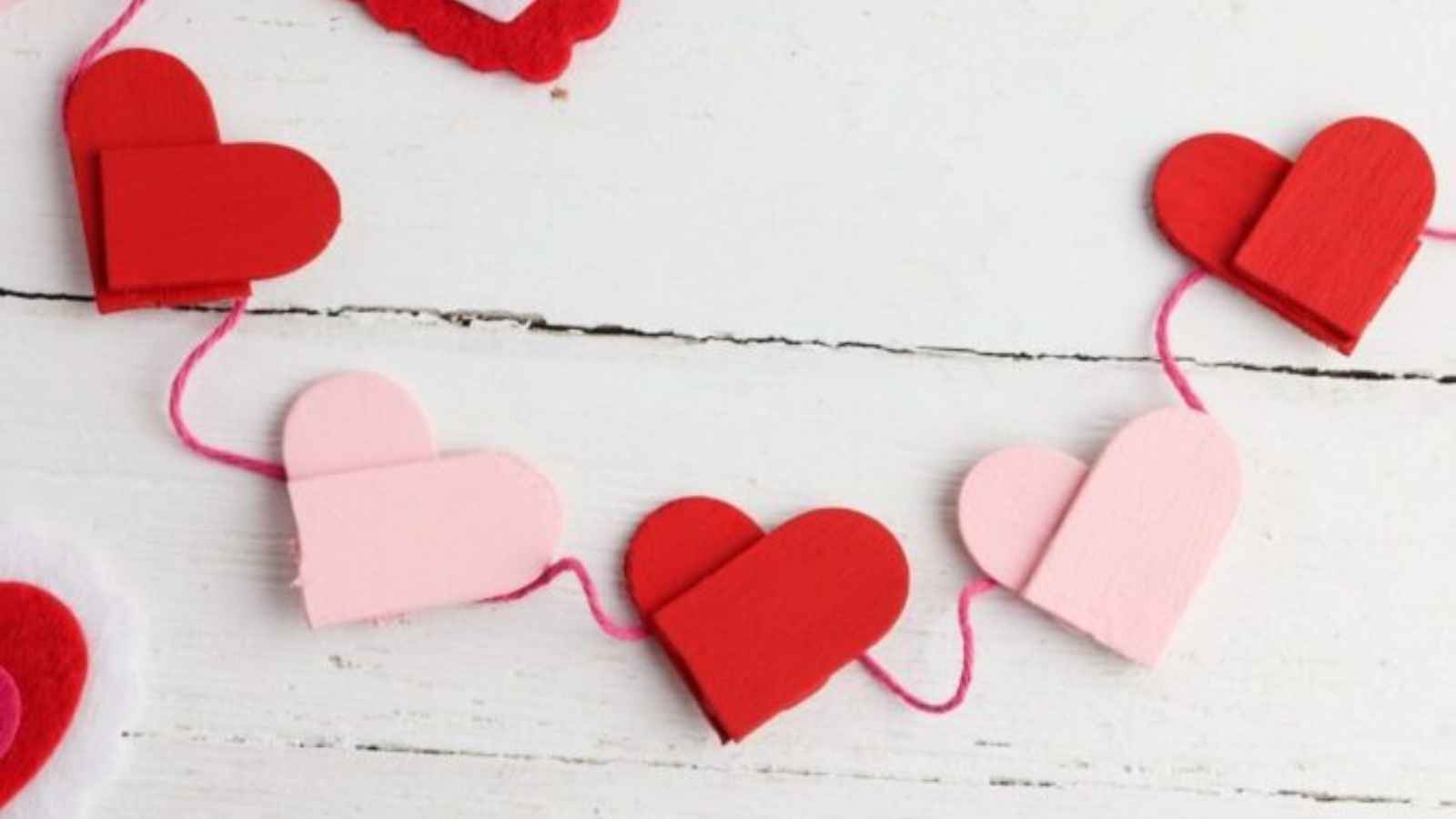 Red and pink wooden hearts are connected by a string, forming a garland on a white wooden surface.