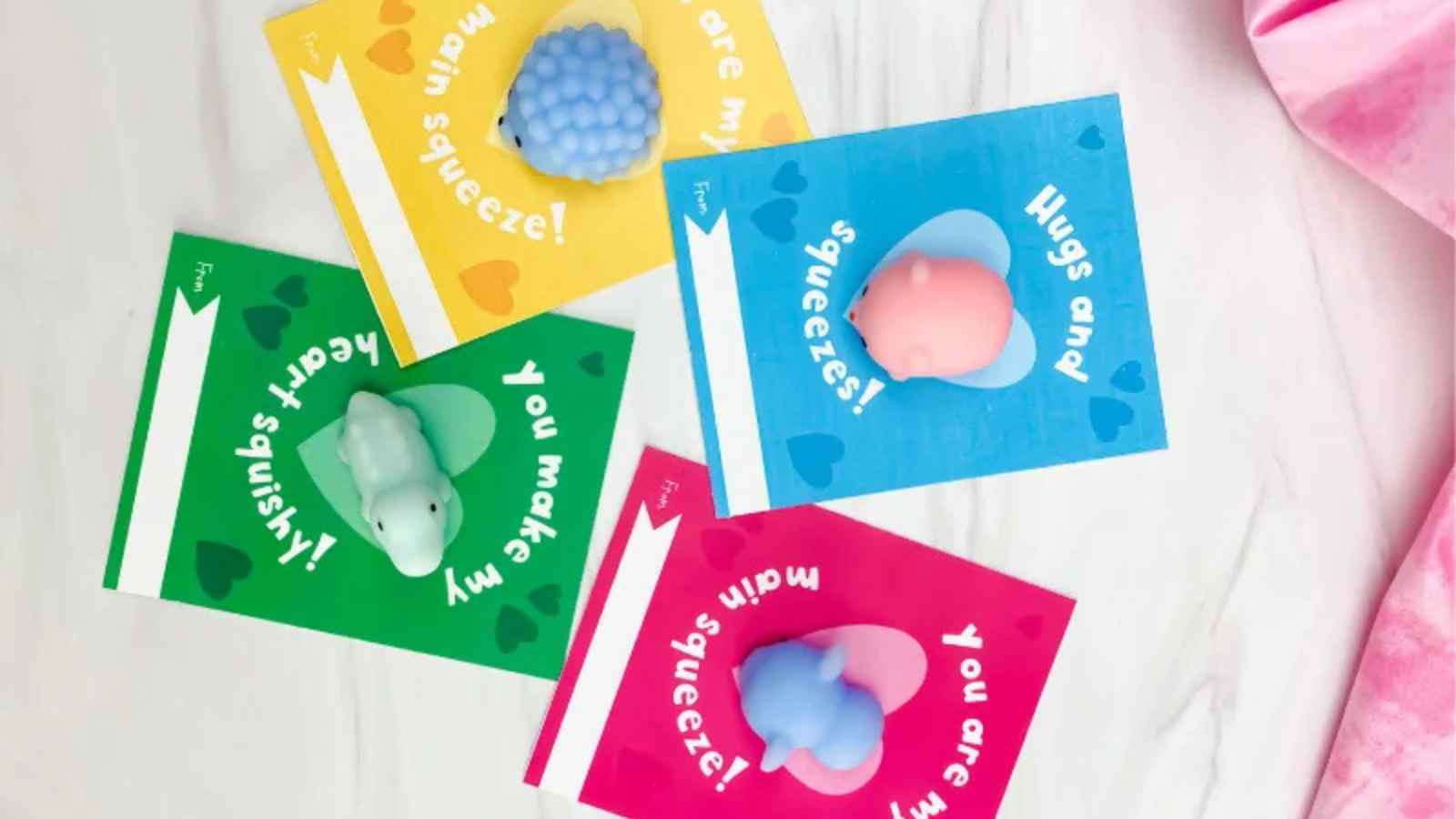 Four colorful cards with heart designs, each featuring a squishy toy animal. Text includes phrases like "Hugs and squeezes!" and "You make my heart squishy!.