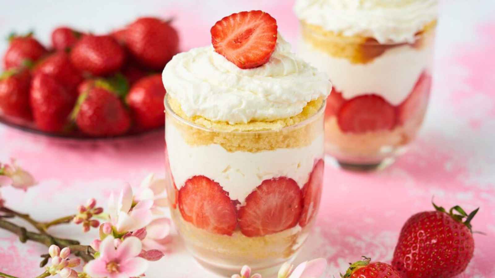 Two glasses of strawberry shortcake parfait with whipped cream, layered with slices of fresh strawberries.