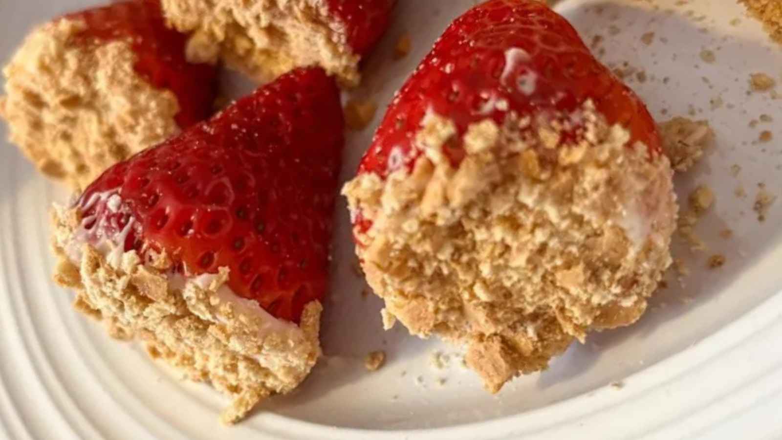 Strawberries coated with crumbled cookies on a white plate.