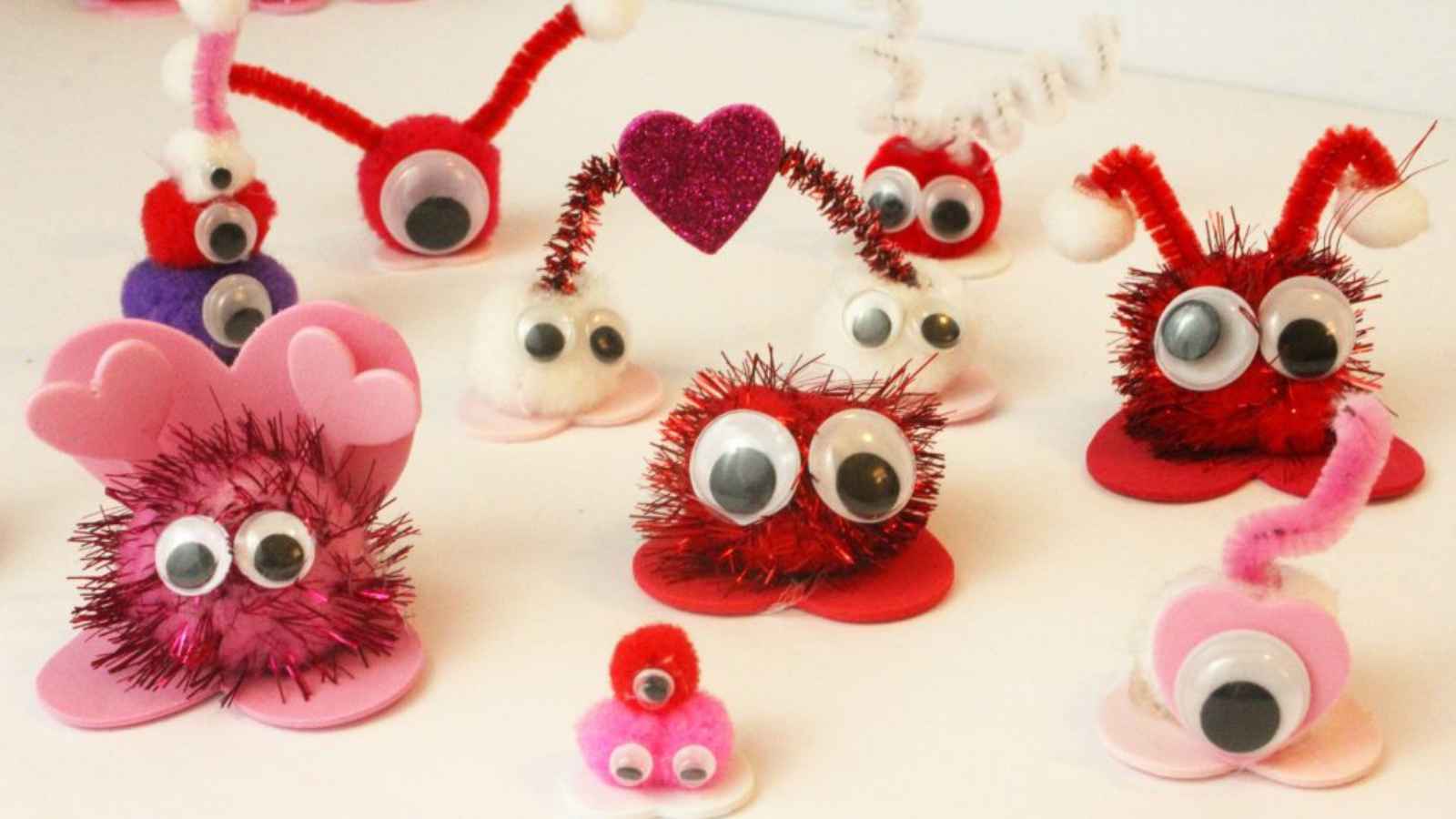 Colorful, fuzzy creatures with googly eyes made from pipe cleaners and pom-poms are arranged on a table.