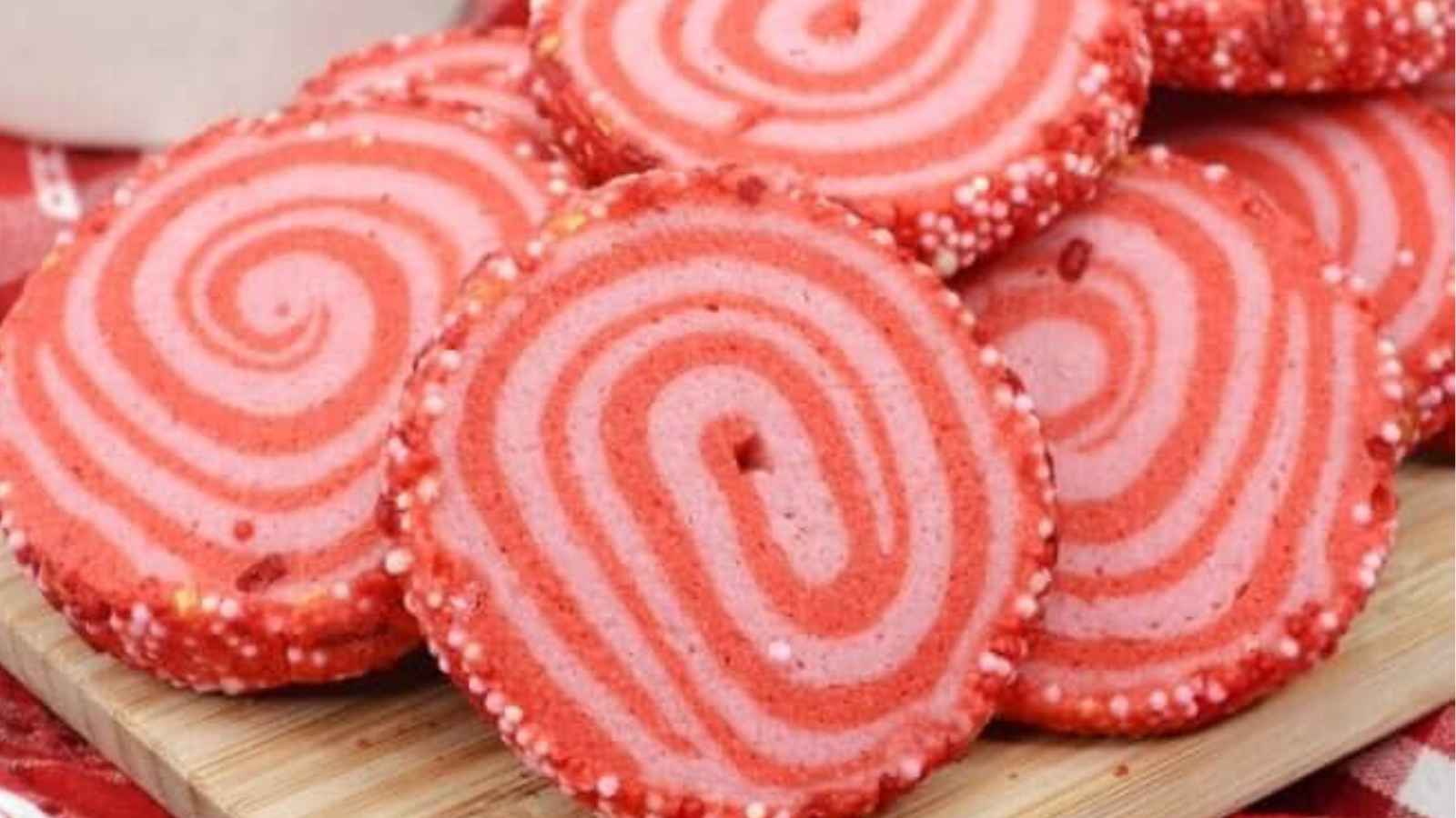 A stack of pink spiral cookies with white and pink sprinkles on the edges, placed on a wooden board.