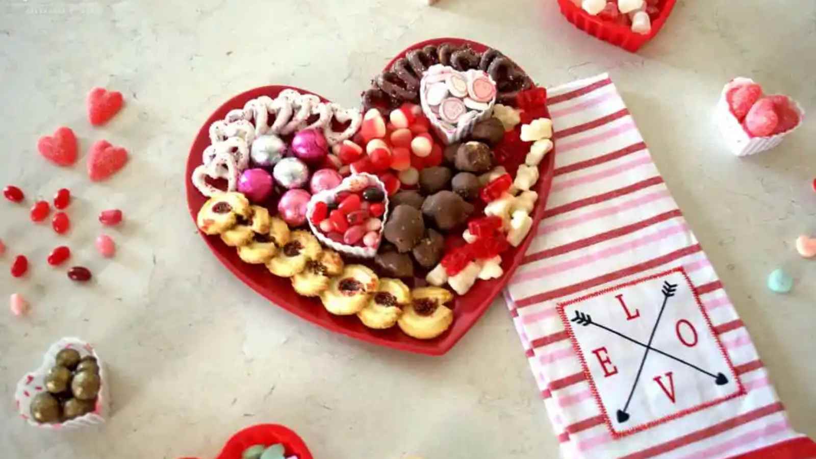 Heart-shaped platter with assorted candies and cookies next to a striped cloth with
