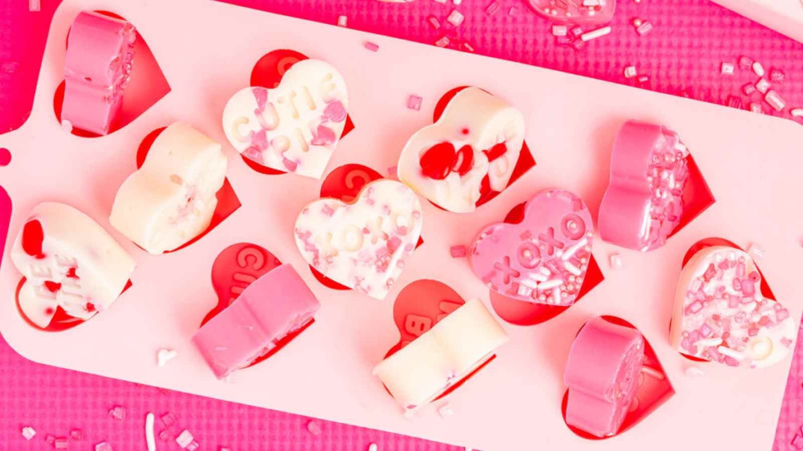 Heart-shaped candies in various colors, decorated with sprinkles and messages like