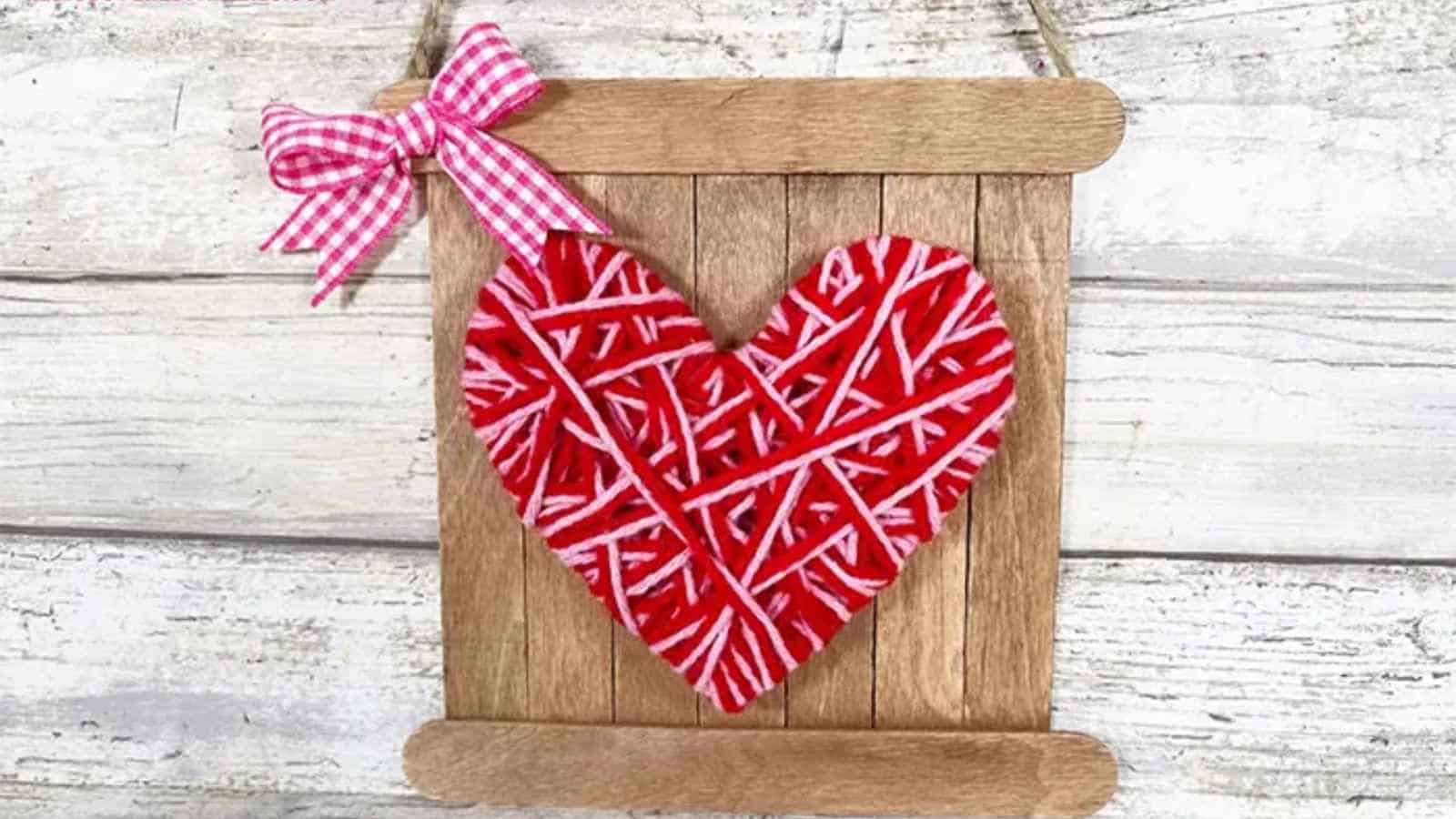 A wooden slat wall hanging with a red and white string-wrapped heart and a pink gingham bow attached.