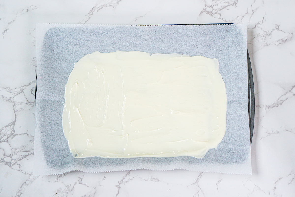 A baking tray lined with parchment paper holds a rectangular layer of white chocolate spread evenly across the surface.