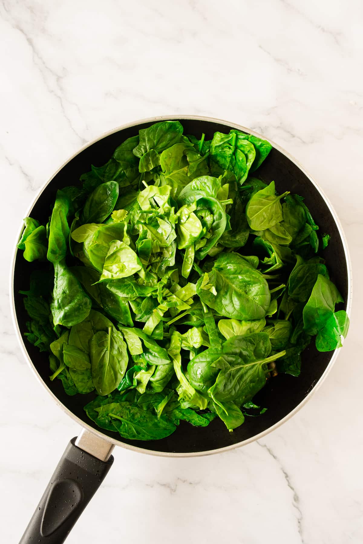 A pan filled with fresh green spinach leaves, ready to transform into a delightful baked spinach cannelloni, rests on a marble surface.