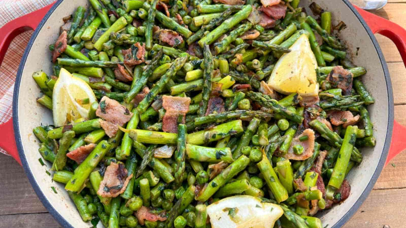 Sautéed asparagus with bacon, peas, and lemon wedges in a red Dutch oven.