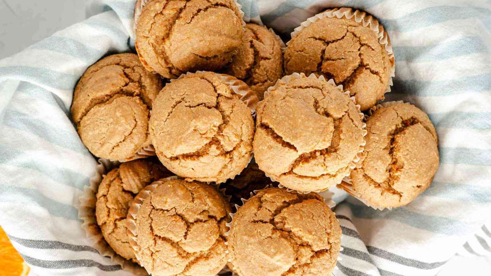 A basket lined with striped cloth contains several freshly baked muffins with cracked tops.