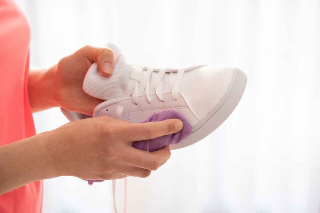 Gently demonstrating how to clean sneakers, a person meticulously wipes a white sneaker with a soft purple cloth, ensuring every inch gleams and the shoe looks as good as new.