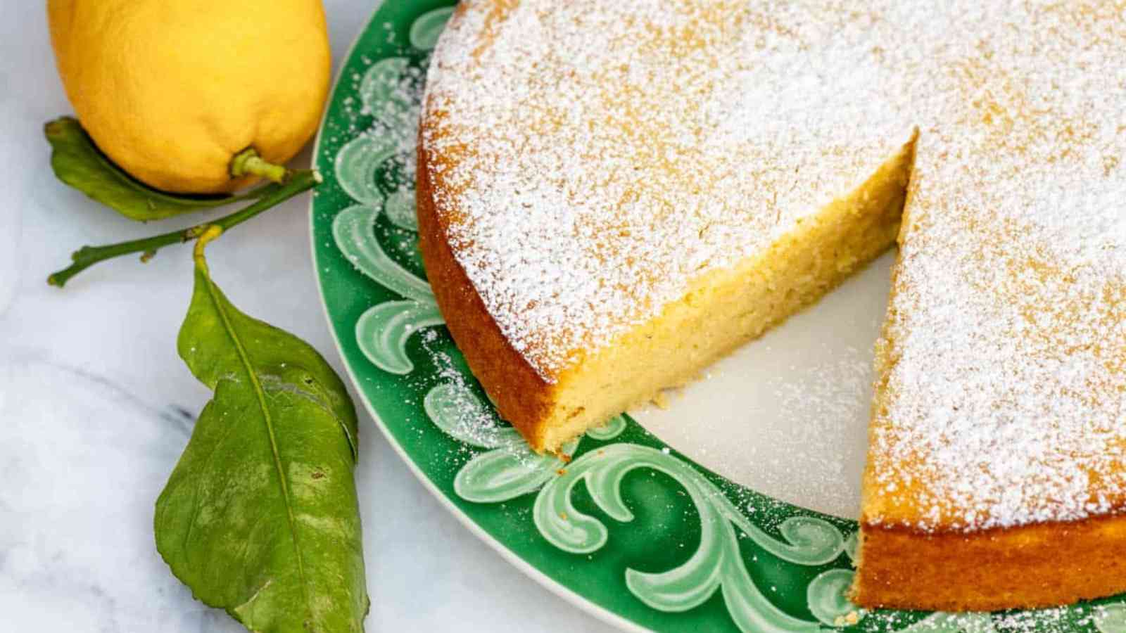 Lemon ricotta cake with a slice taken out on a plate next to a lemon.