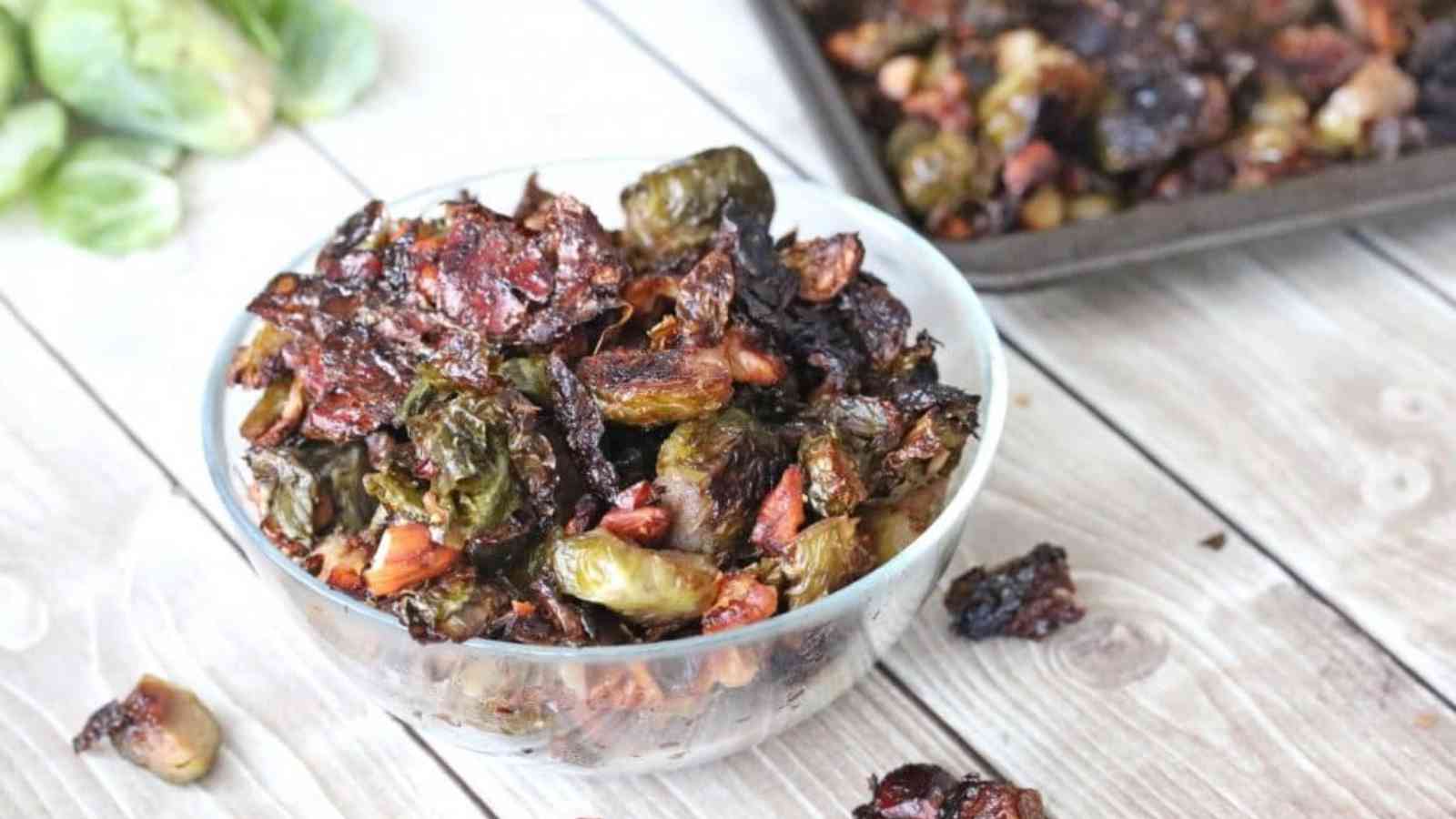 Glass bowl with roasted brussels sprouts and more sprouts on a baking tray behind it.