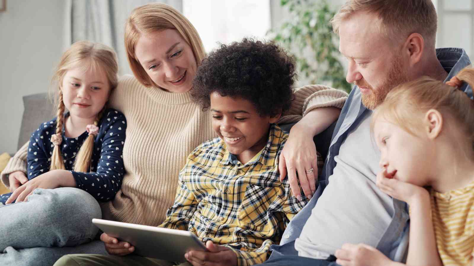 Family of five sitting on a couch, looking at a tablet together.