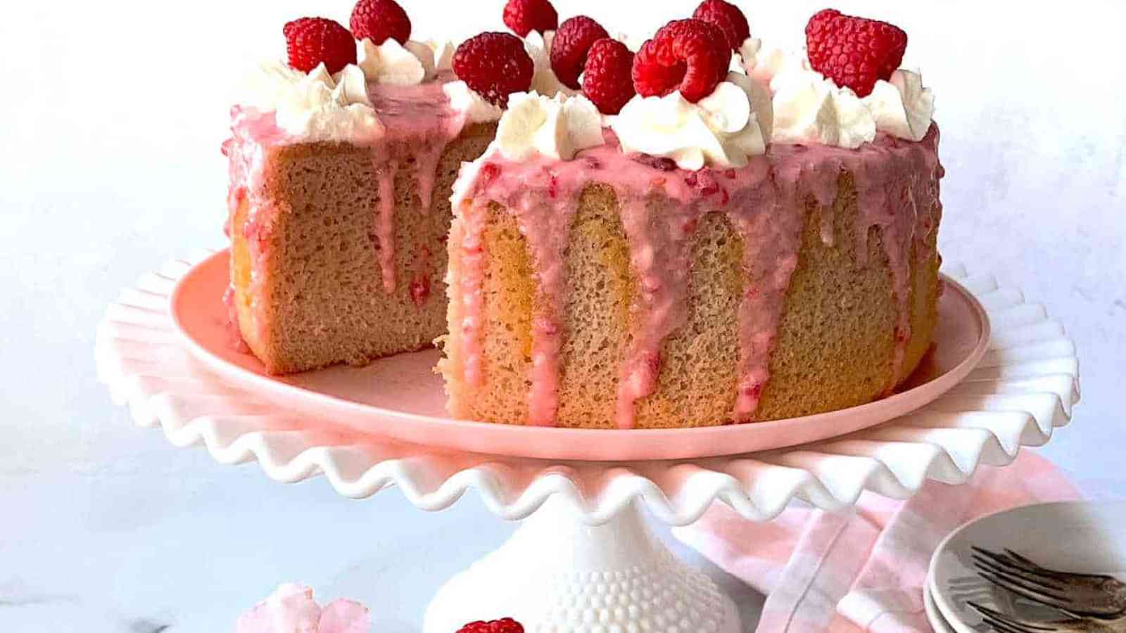 Raspberry cake on a white stand with plates and napkins.