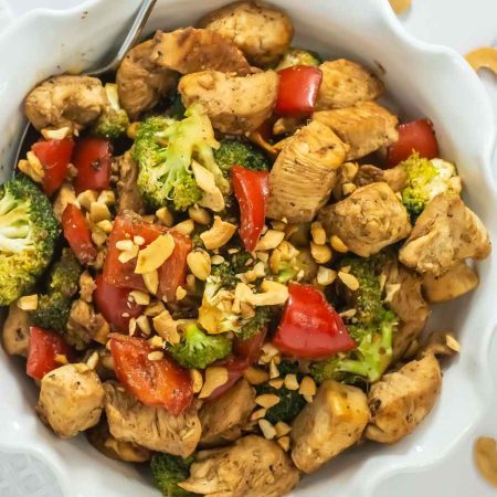 A delicious chicken cashew and broccoli stir fry, featuring a bowl of tender chicken with crunchy broccoli, vibrant red bell peppers, and savory cashews on a plate,