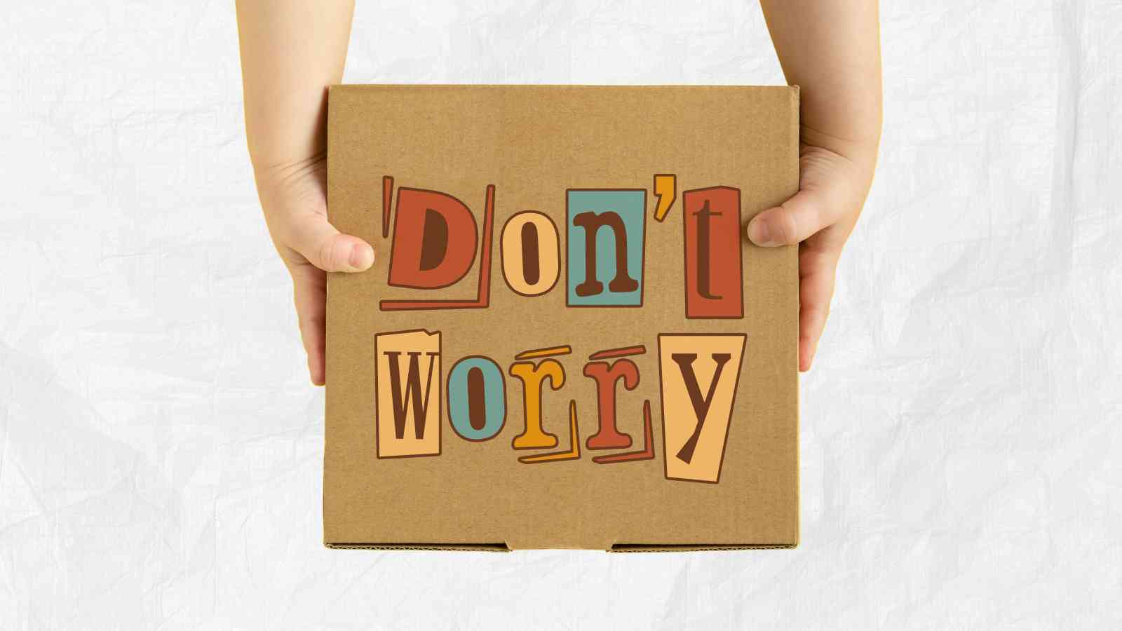 Hands holding a cardboard box with the text "Don't Worry" in colorful letters on the front. The background is plain white.