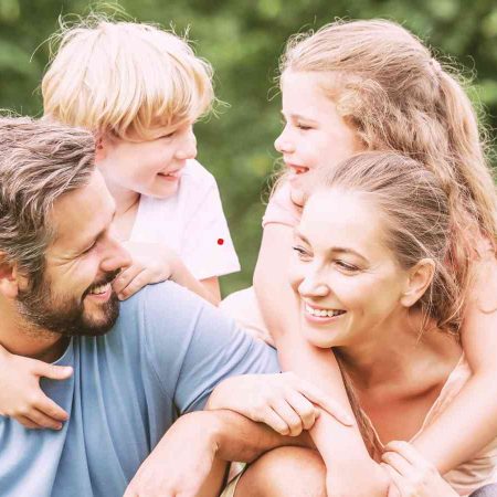 Two adults smiling and hugging a child outdoors.