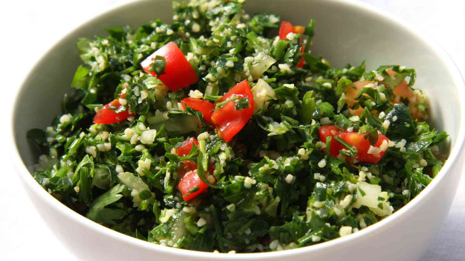 A bowl of tabbouleh salad containing chopped parsley, mint, tomatoes, bulgur, and onions.