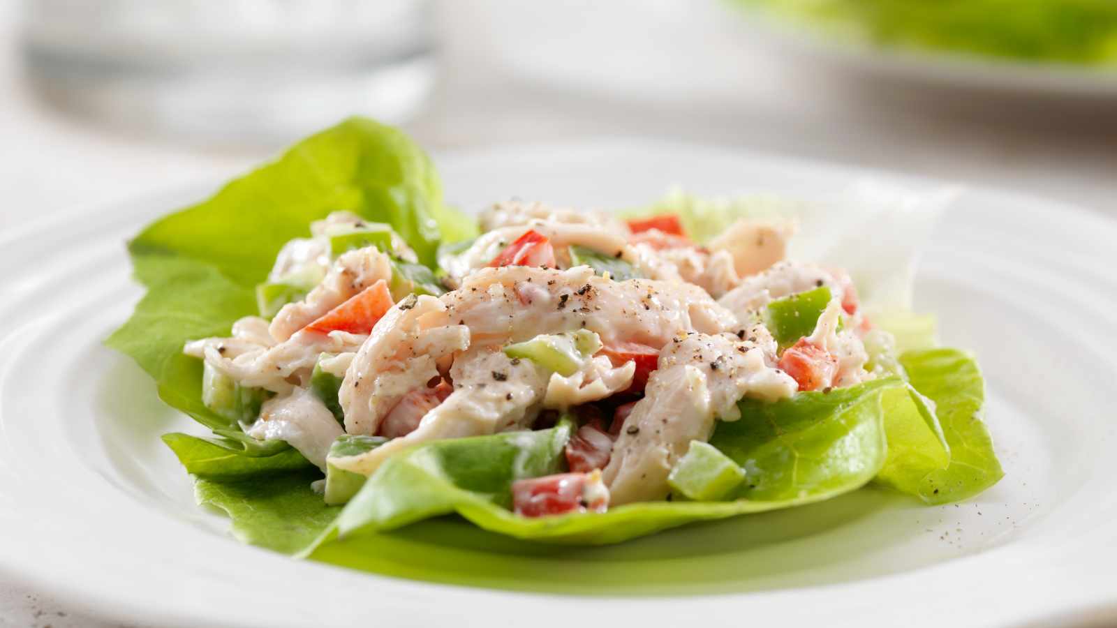 Chicken salad with diced red and green peppers, served on a bed of lettuce and garnished with black pepper, on a white plate.