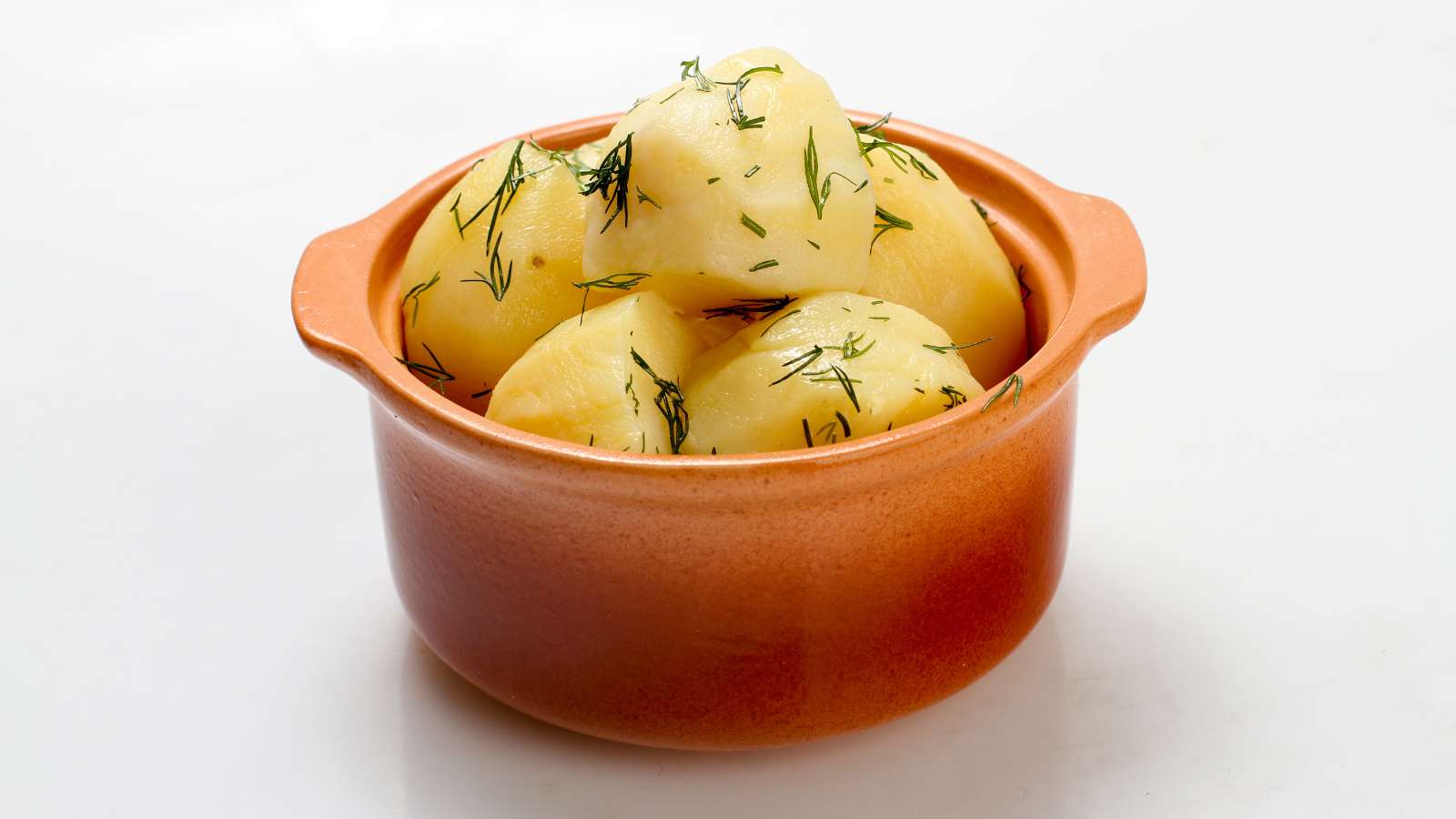 Boiled potatoes garnished with dill in an orange ceramic pot on a white background.