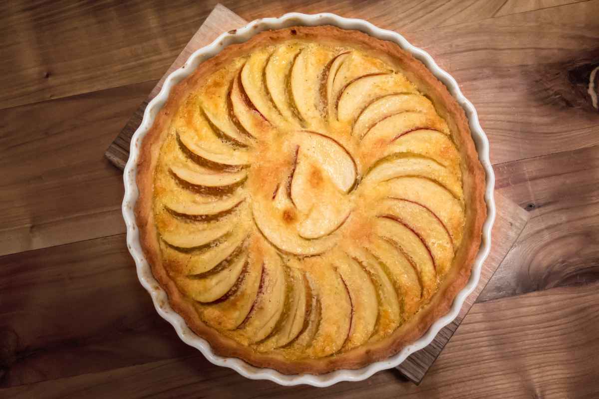 A baked apple tart with circularly arranged apple slices on a wooden surface.