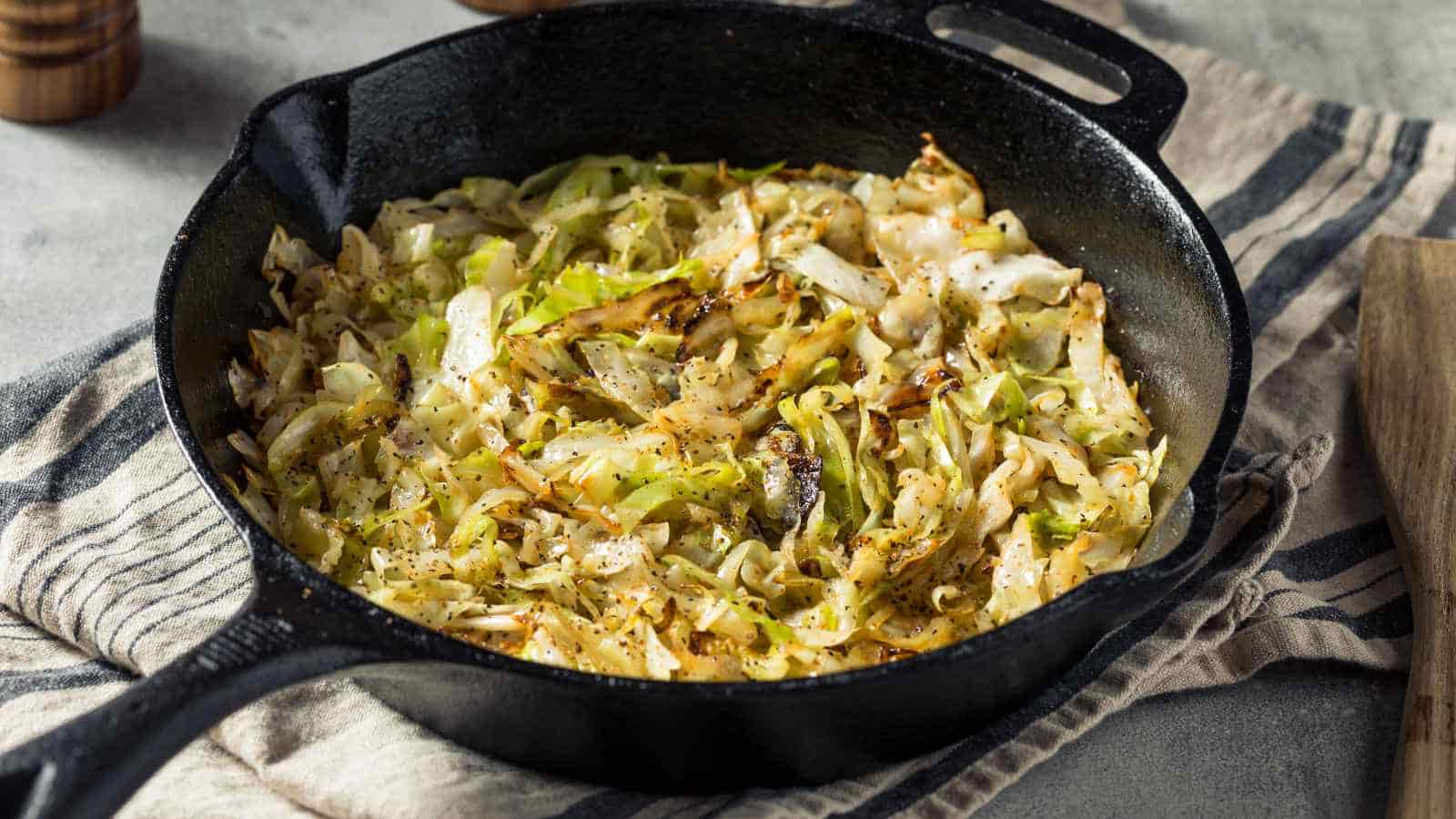 A cast iron skillet filled with cooked shredded cabbage, seasoned and slightly browned, placed on a striped cloth.