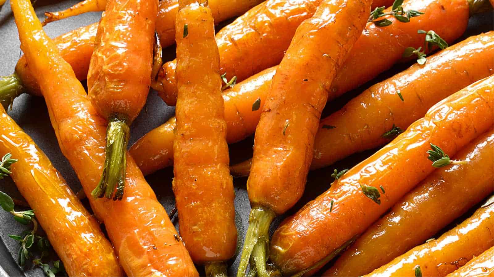 A close-up of roasted carrots glistening with olive oil and garnished with small herb sprigs.