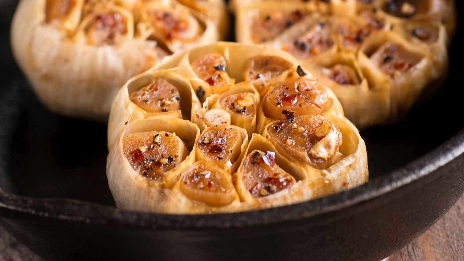 Roasted garlic bulbs in a black cast iron pan, seasoned with cracked pepper and spices.