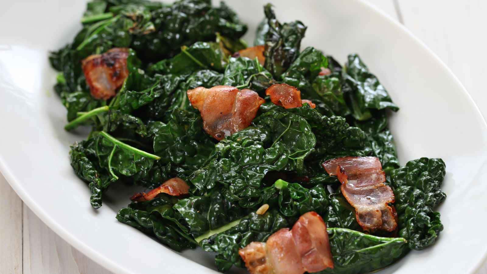 A white plate with kale salad and crispy bacon pieces.