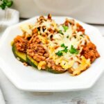 A serving of ground beef and zucchini casserole lasagna topped with melted cheese and parsley on a white plate.