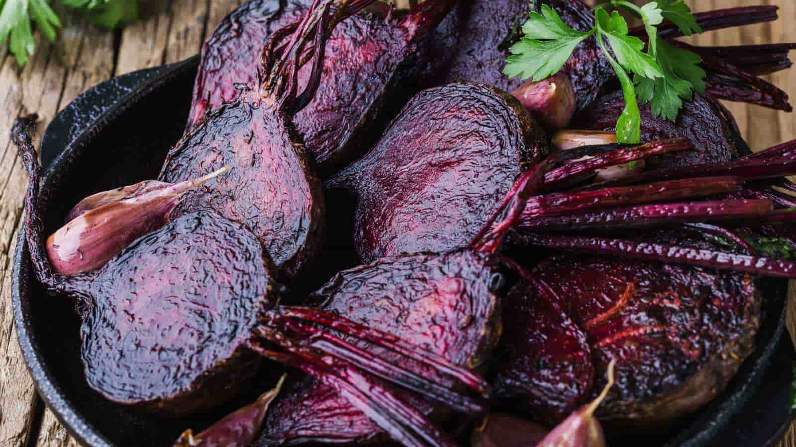 Roasted purple beets and garlic cloves in a black skillet, garnished with parsley.